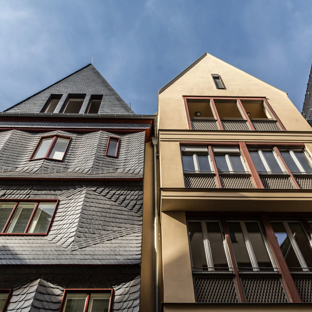 Facade view of modern buildings in Frankfurt’s new old town between the cathedral and the Römer, featuring slate roofs and clean geometric shapes under a blue sky